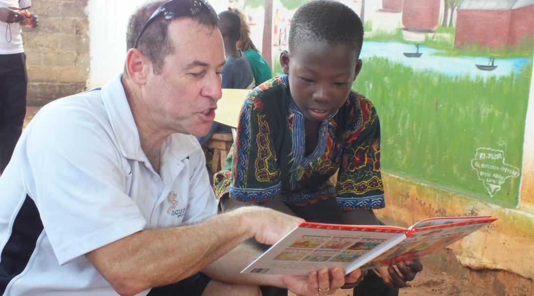 A senior male volunteer helps a child with reading in English at a Childcare Project abroad. An older man volunteering abroad helps a local child improve his reading at one of our Childcare Projects.